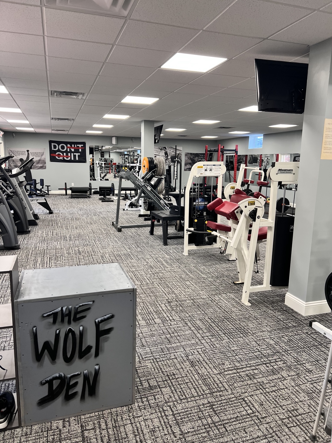 Wolf Den gym floor with strength machines, racks, and the Wolf Den sign